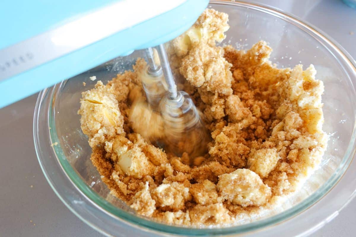 A stand mixer creams sugar, light brown sugar and butter in a glass bowl.