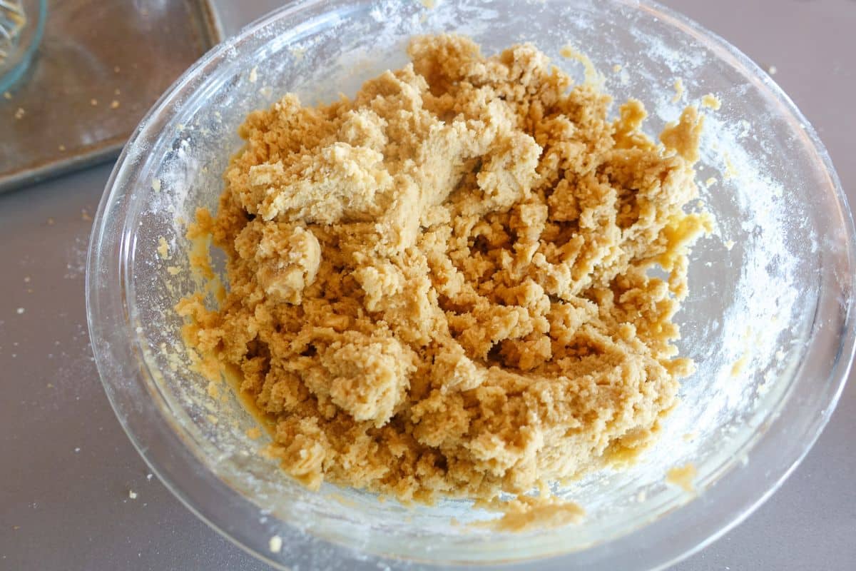 A glass bowl filled with mixed cookie dough sits on a countertop, with some flour scattered around the edge.