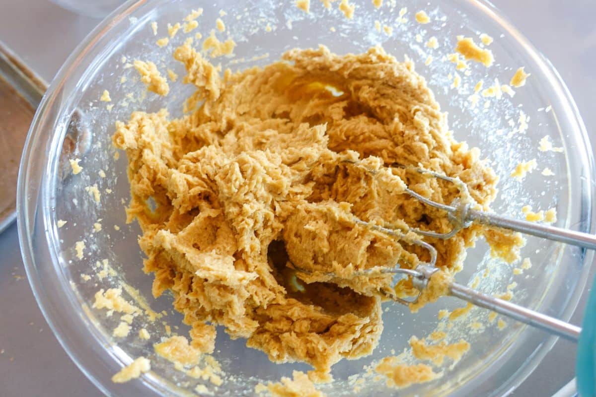 A glass bowl containing partially mixed cookie dough with a hand mixer resting in the mixture.