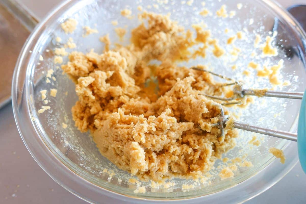 A glass bowl containing creamed butter and sugar mixture with a hand mixer resting inside.