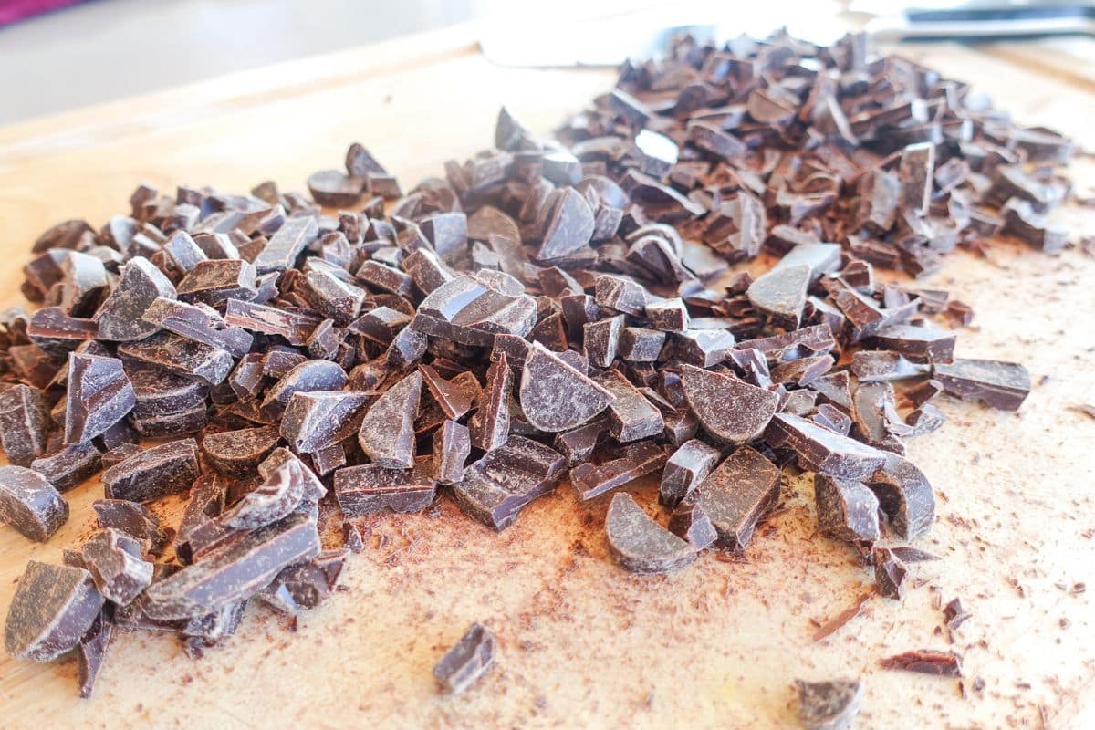 Chopped Valrhona dark chocolate pieces scattered on a wooden cutting board.