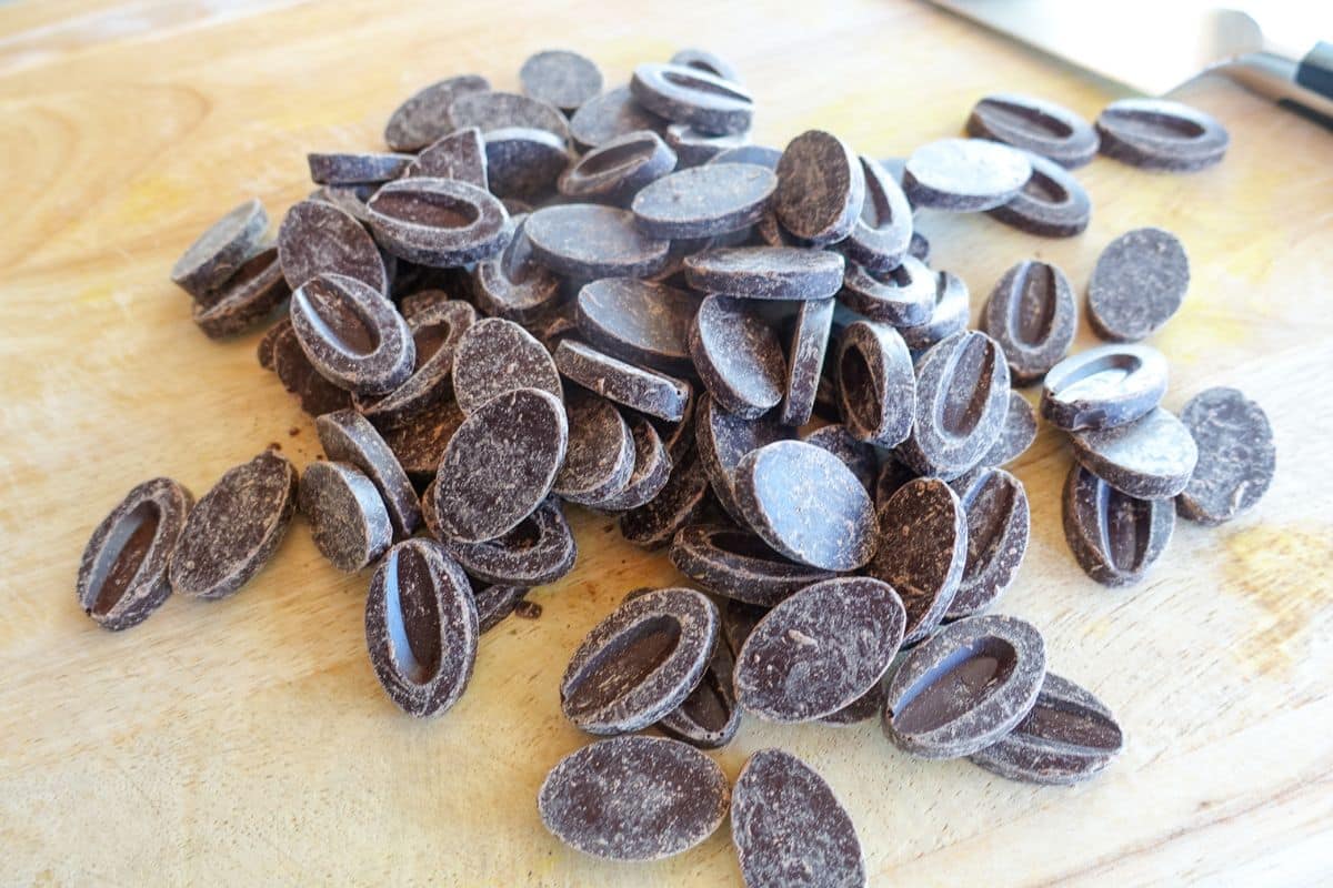 A pile of oval-shaped Valrhona dark chocolate pieces on a wooden surface.