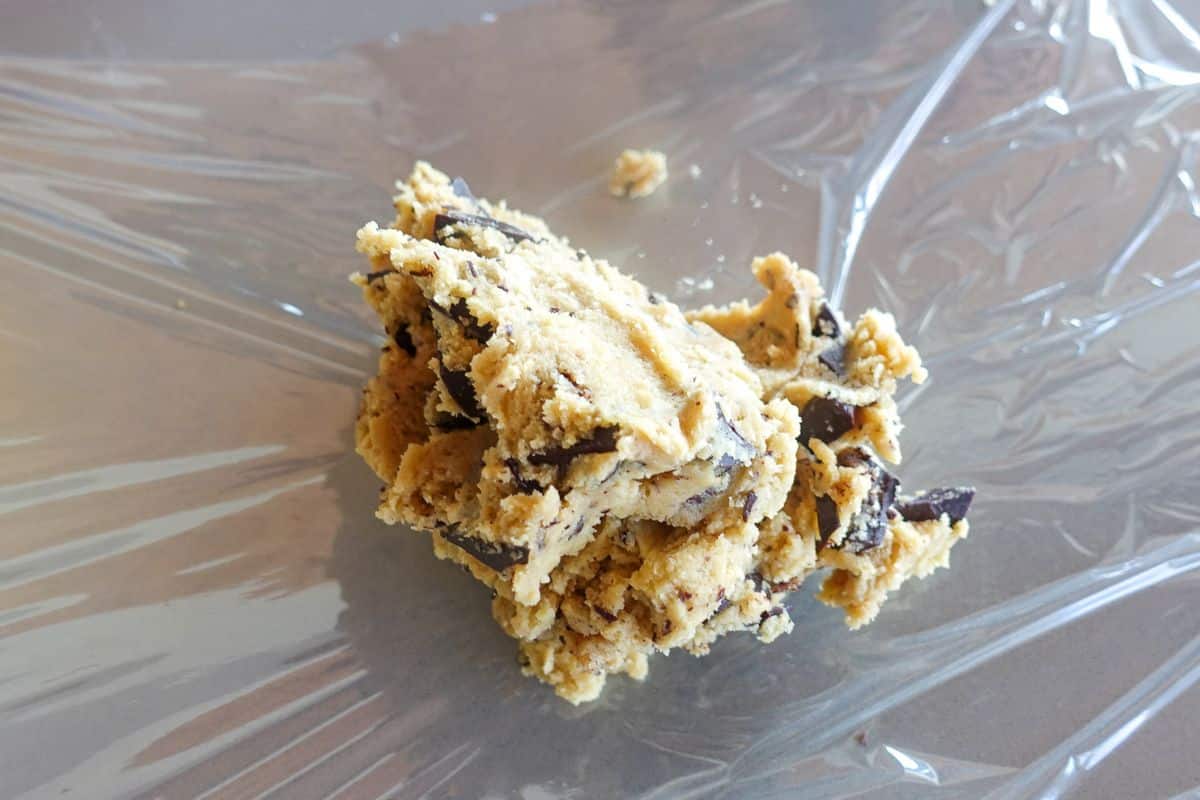 A mound of chocolate chip cookie dough rests on a sheet of plastic wrap.