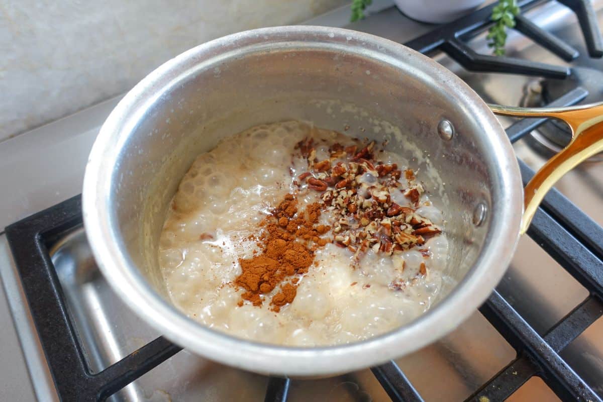 A pot of oatmeal cooking on a stove with cinnamon and chopped nuts sprinkled on top.