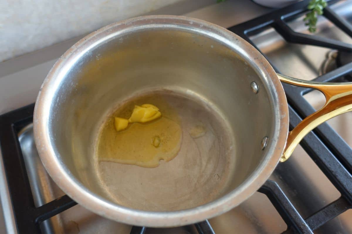 A small amount of ghee melting in a saucepan on a stovetop.