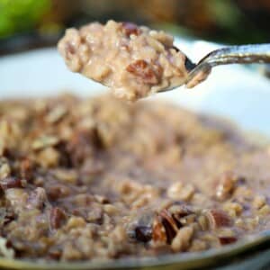 A close-up of a spoonful of date oatmeal with chopped nuts above a bowl filled with the same oatmeal mixture.