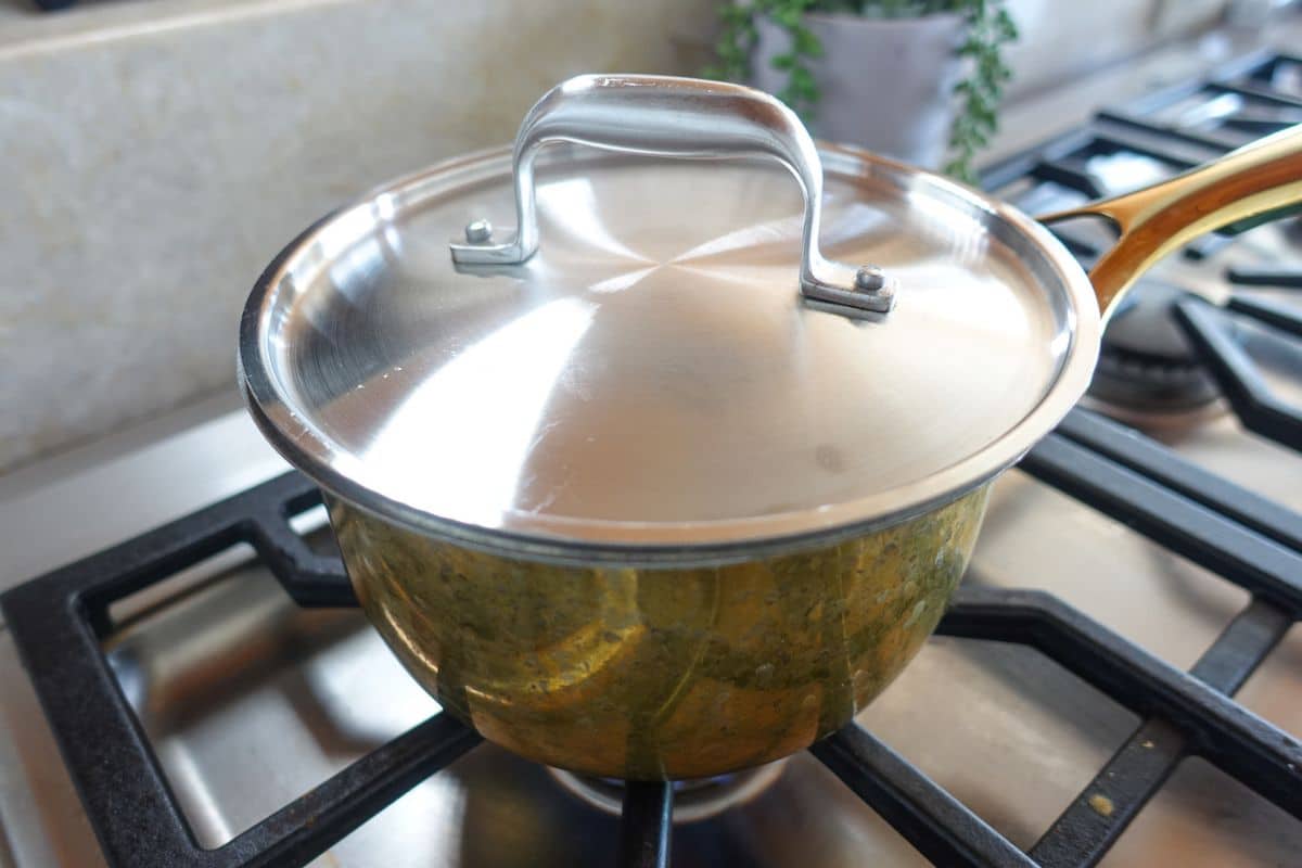A stainless steel pot with a lid sits on a gas stove burner in a kitchen.