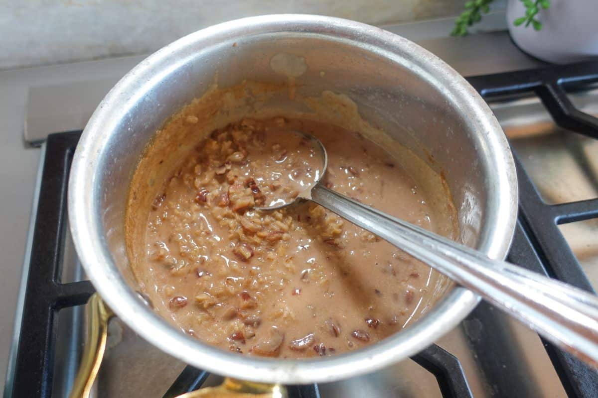 A pot of oatmeal with visible nuts, being stirred with a metal spoon on a stove.