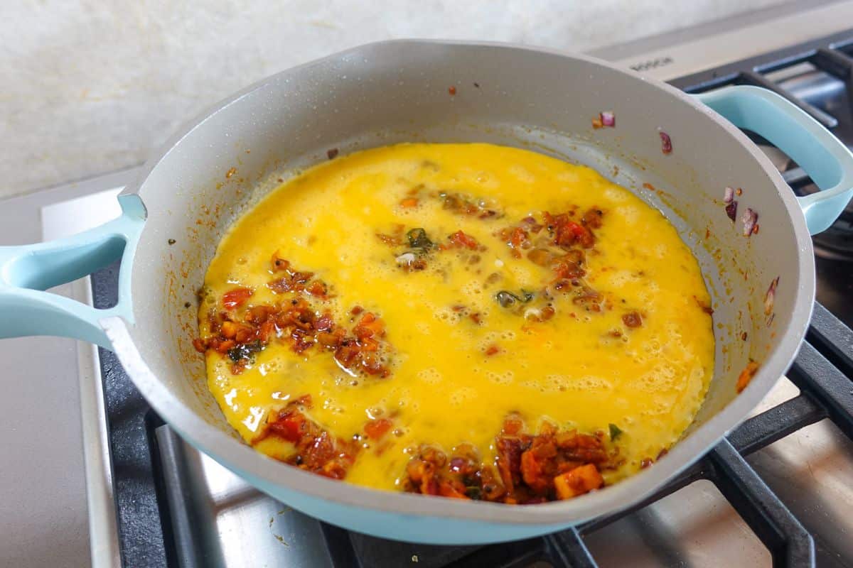 Eggs have been poured over a tomato onion masala mixture to make egg bhurji in a pan.