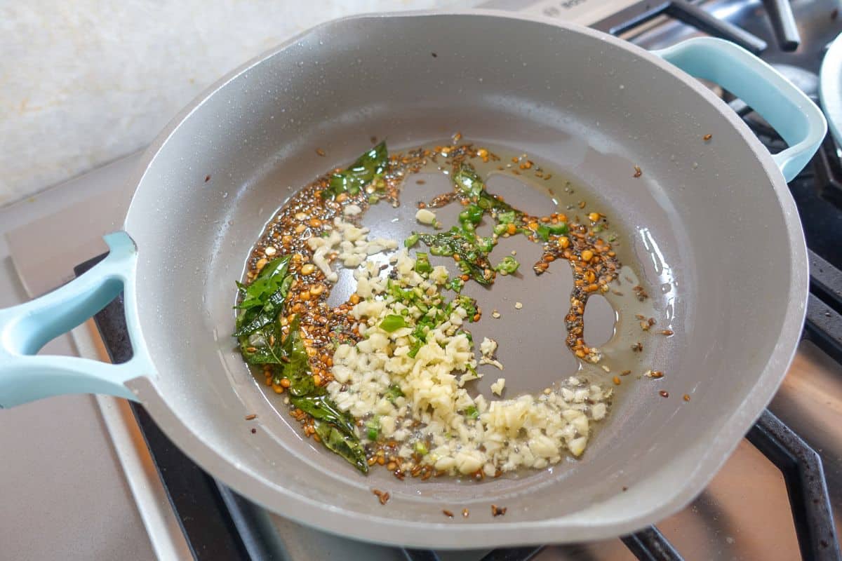 In a nonstick pan there is oil with sauteed whole spices, curry leaves, and chopped garlic.