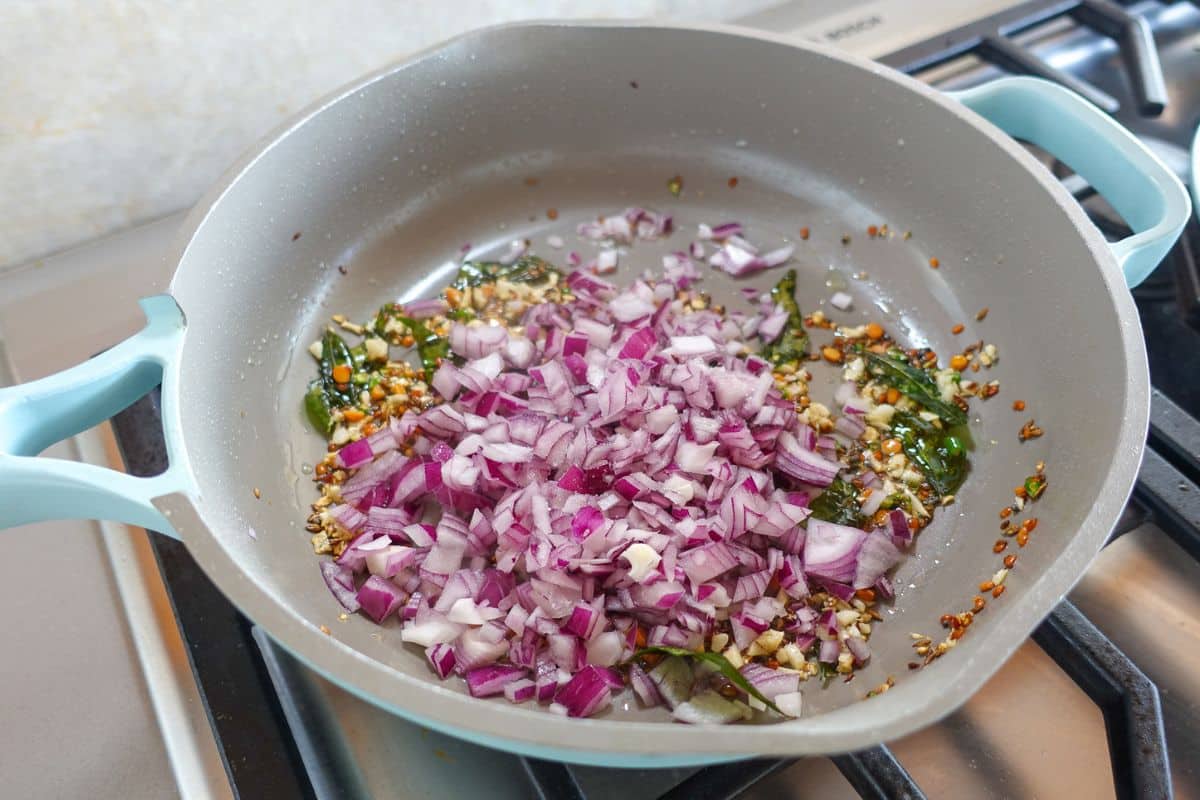 Chopped red onions have been added to a pan with curry leaves, garlic, and sauteed spices.