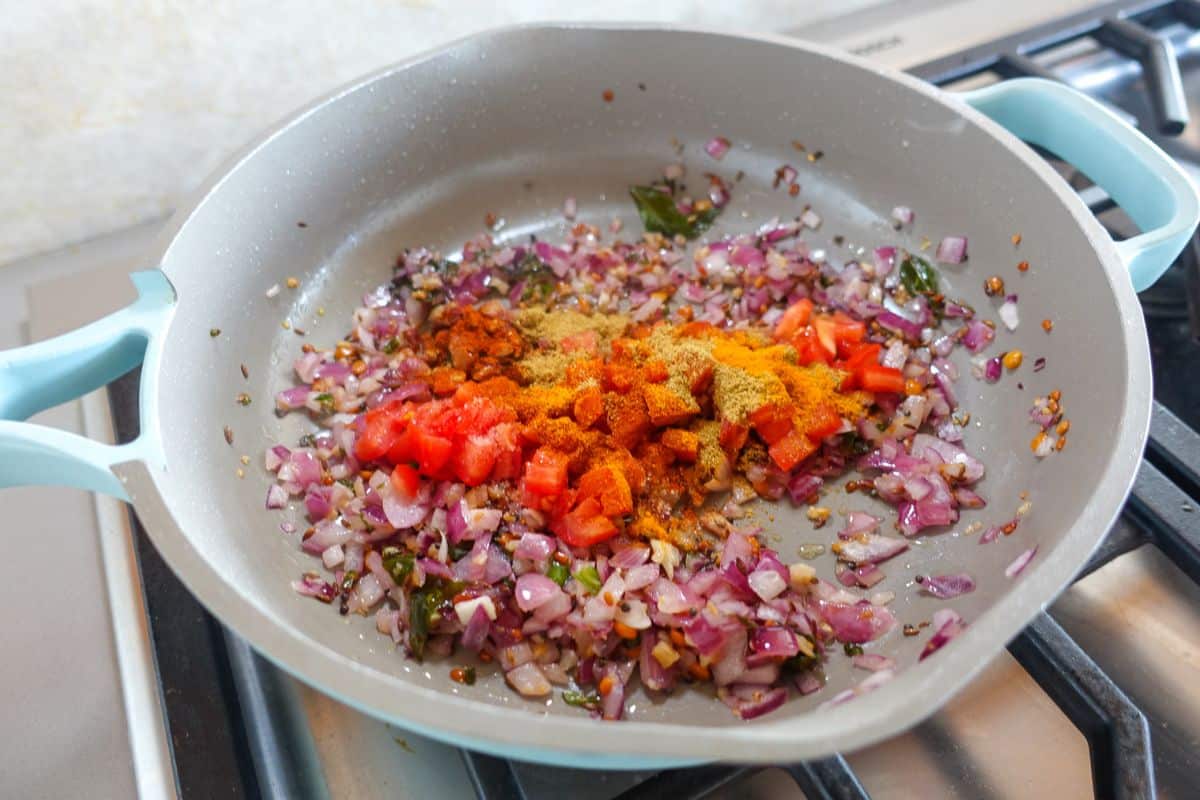 Chopped tomatoes and ground spices added to sauteed onions in a pan.