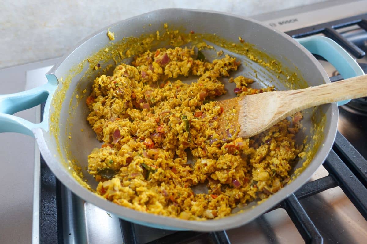 Scrambled egg bhurji with a wooden spoon inside a pan.