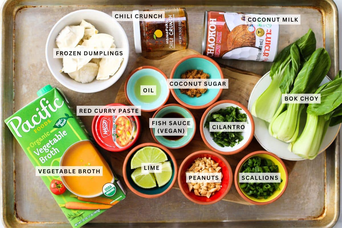 A tray containing labeled ingredients for a recipe, including frozen dumplings, bok choy, vegetable broth, red curry paste, oil, coconut sugar, chili crunch, coconut milk, lime, peanuts, scallions, cilantro, and vegan fish sauce.