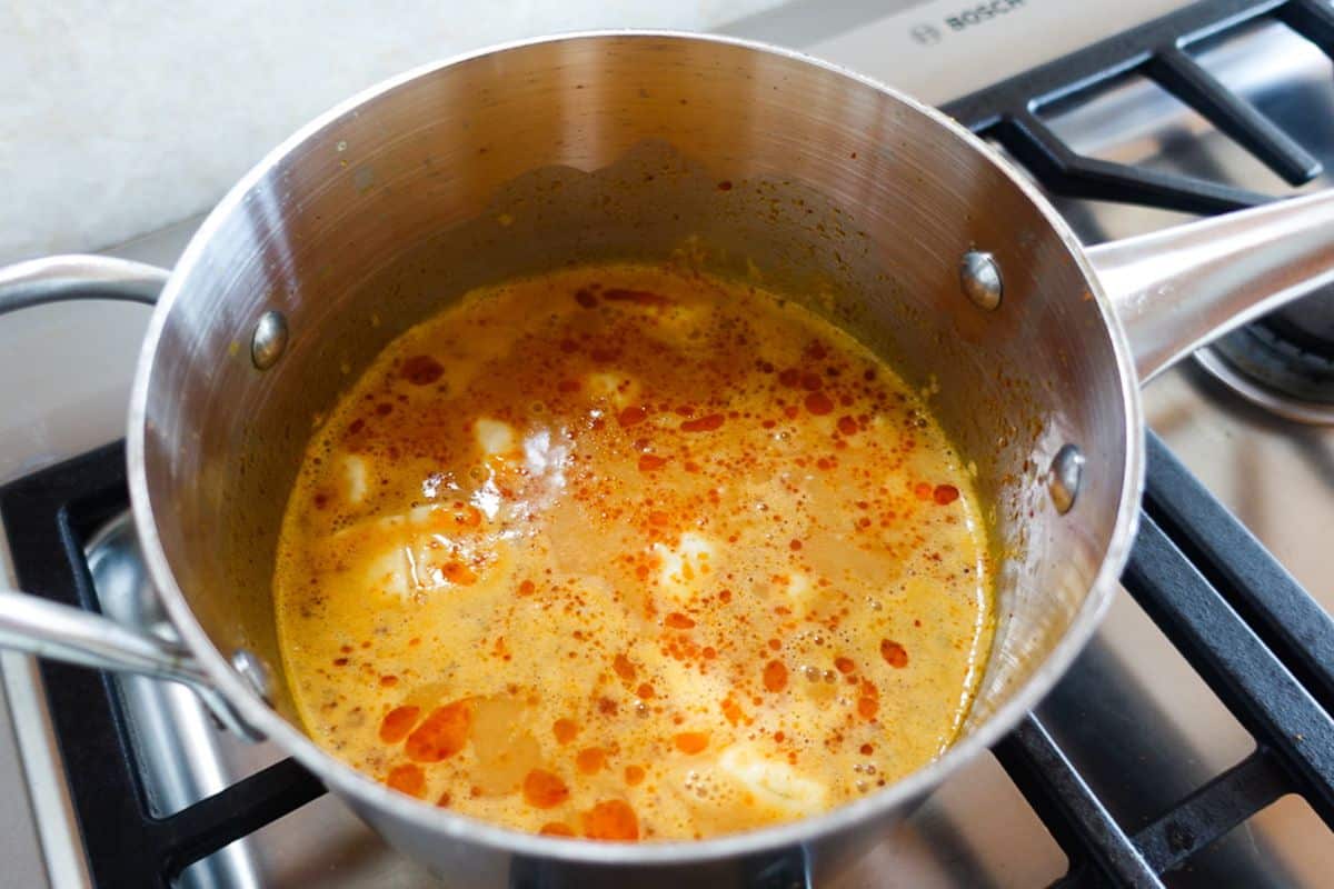 A stainless steel pot on a stove contains a simmering yellow-orange soup with frozen dumplings on the surface.