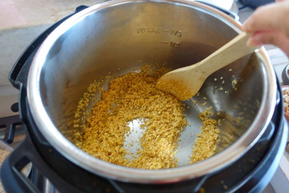A wooden spoon stirs saut&eacute;ed cracked wheat in an Instant Pot