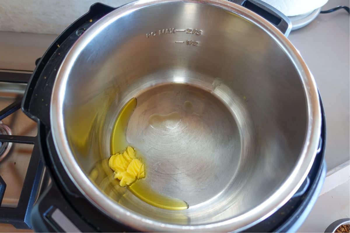 A close-up of an empty stainless steel Instant pot with a small amount of ghee melting at the bottom.