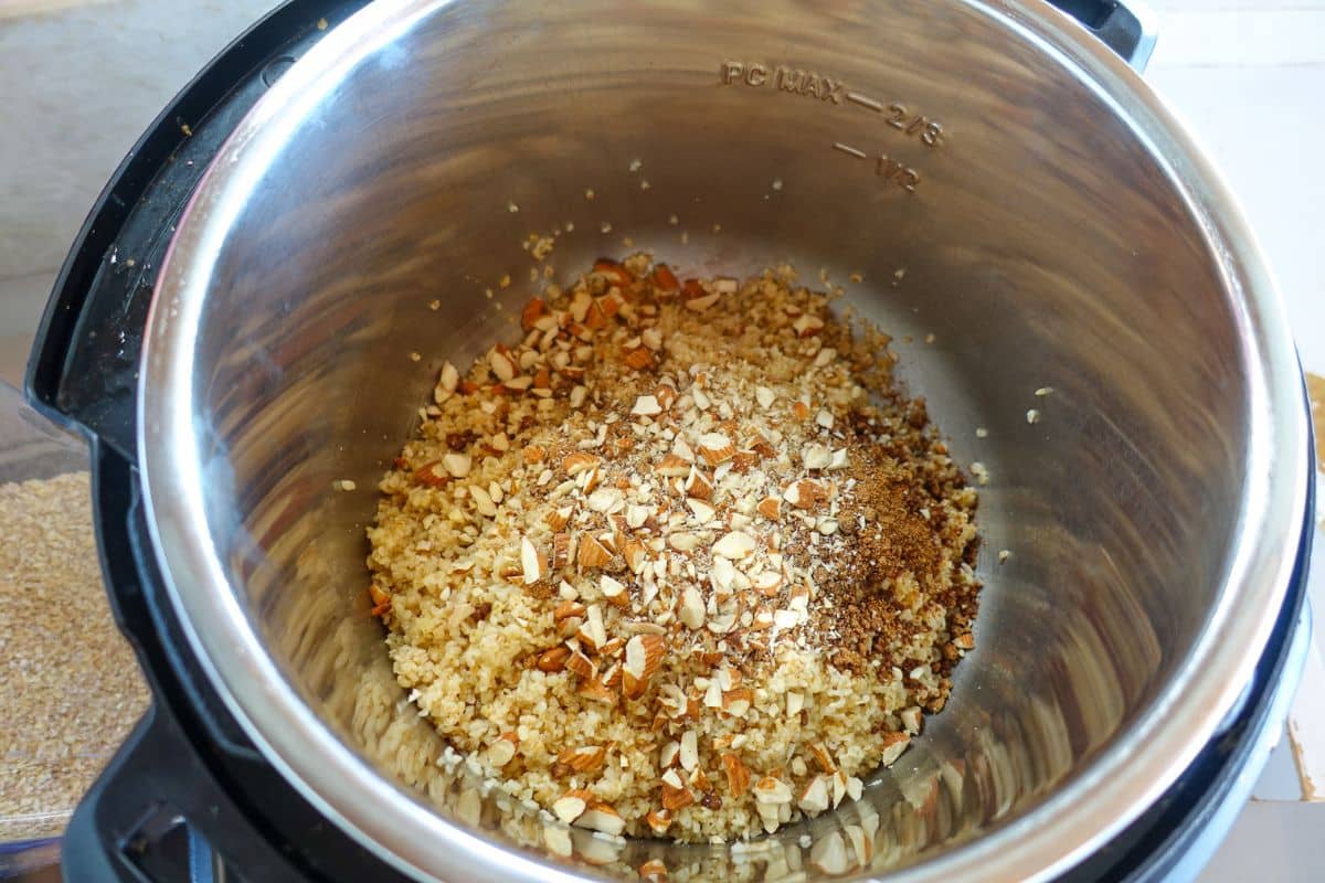 Cooked daliya topped with chopped almonds and jaggery in a stainless steel Instant Pot.