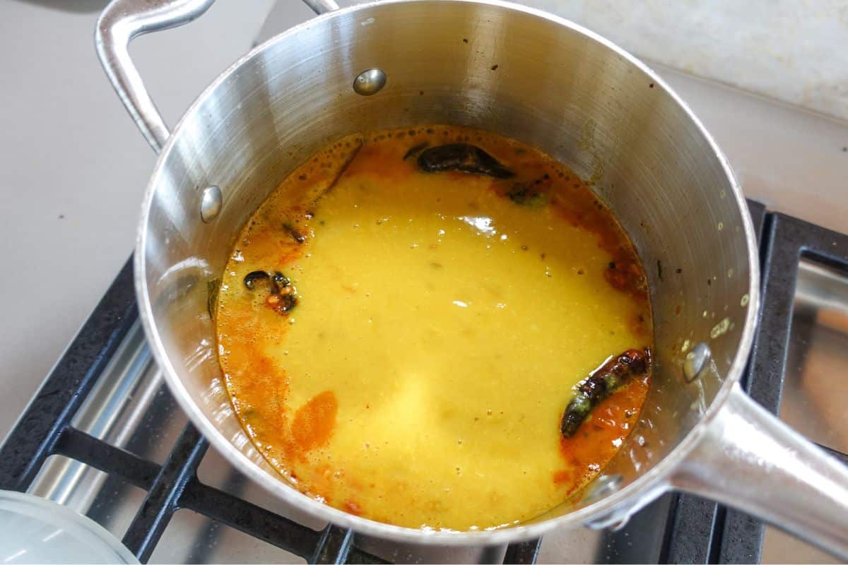 A stainless steel pot on a stove containing toor dal with visible spices and oil on the surface.