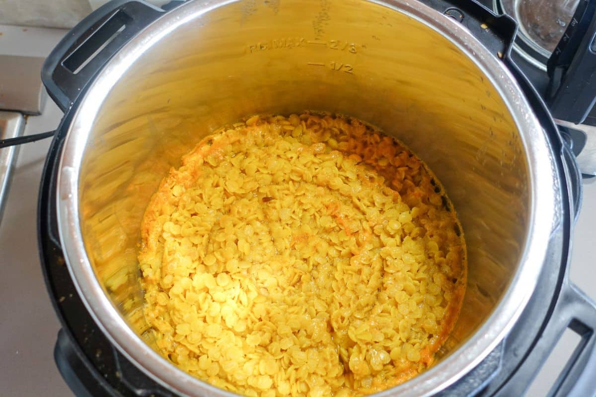 Cooked yellow lentils in an Instant Pot pressure cooker, with the lid removed, showing a layer of cooked lentils and some liquid.