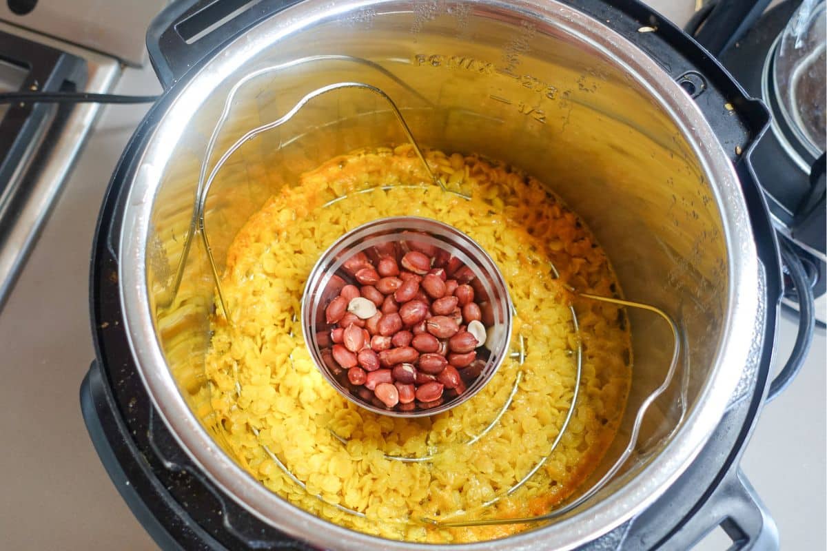Instant Pot with cooked yellow lentils at the bottom and a small metal bowl of dry peanuts placed in the center on a steaming rack.