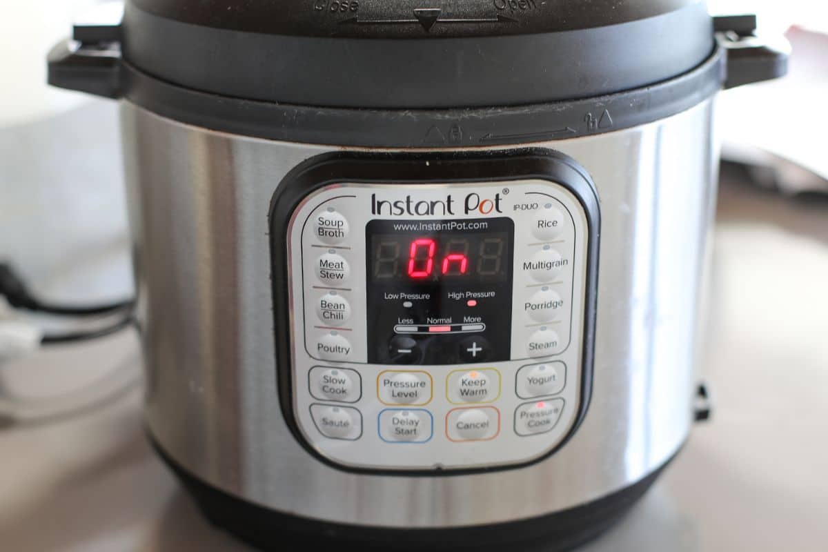 A stainless steel Instant Pot electric pressure cooker displays On on its digital screen, with various cooking options visible on the control panel.