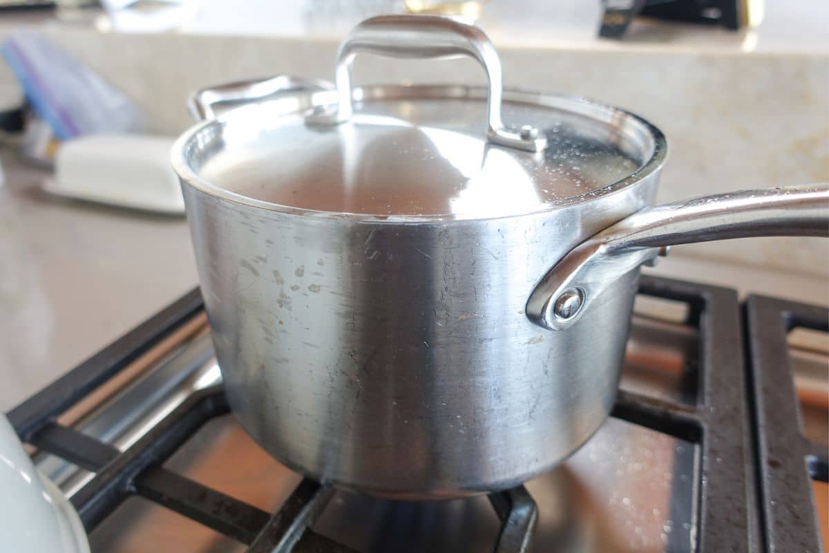 A stainless steel pot with a lid is heating on a gas stove burner in a kitchen.