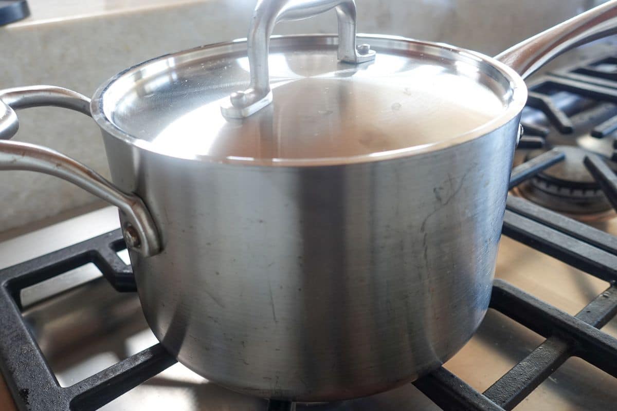 A stainless steel pot with a lid sits on a gas stove burner.