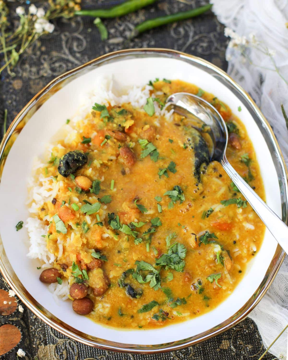 A bowl of rice topped with Gujarati dal, garnished with chopped cilantro, with a spoon resting in the bowl.