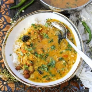 A bowl of rice topped with Gujarati Dal garnished with cilantro, next to a serving bowl filled with more Gujarati Dal, with green chilies on the side.