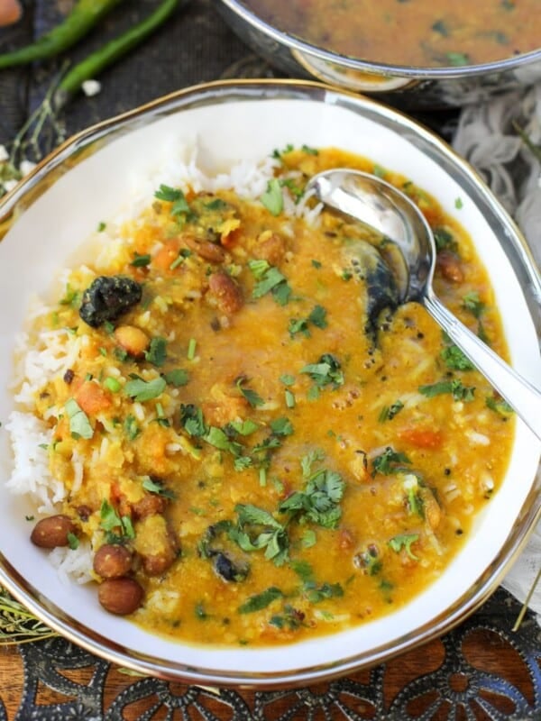 A bowl of rice topped with Gujarati Dal garnished with cilantro, next to a serving bowl filled with more Gujarati Dal, with green chilies on the side.