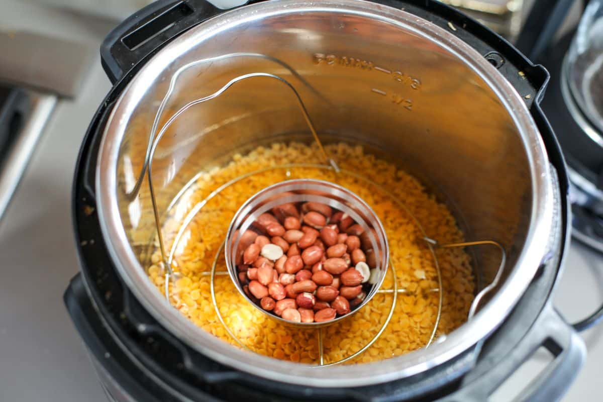 Instant Pot containing yellow split lentils at the bottom and a smaller bowl with raw peanuts placed on a trivet inside.