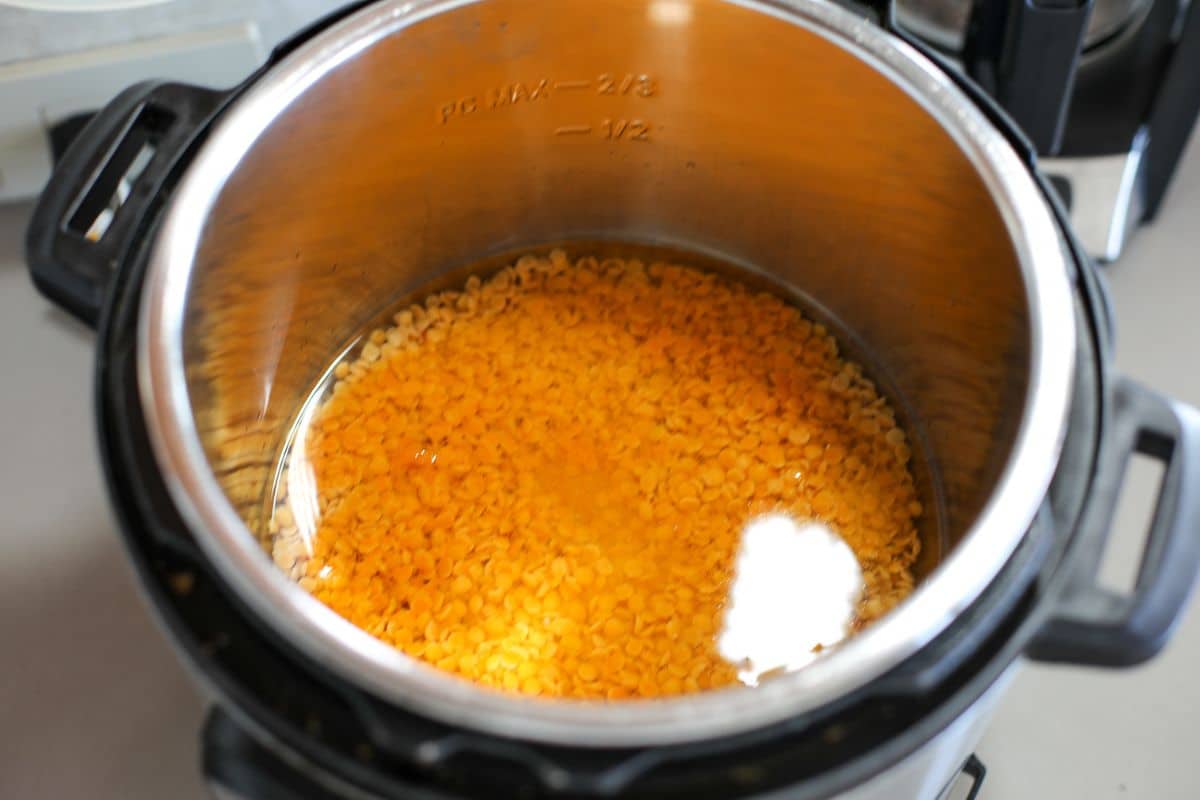 An Instant Pot containing yellow lentils, turmeric powder, and water is shown before cooking.