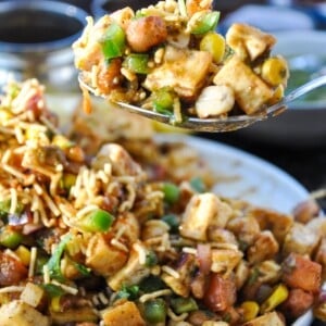A close-up of a spoonful of tofu chaat with diced tofu, peanuts, corn, green peppers, sev, and spices, served on a plate.