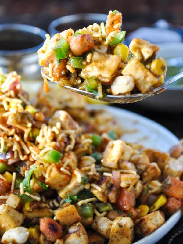 A close-up of a spoonful of tofu chaat with diced tofu, peanuts, corn, green peppers, sev, and spices, served on a plate.