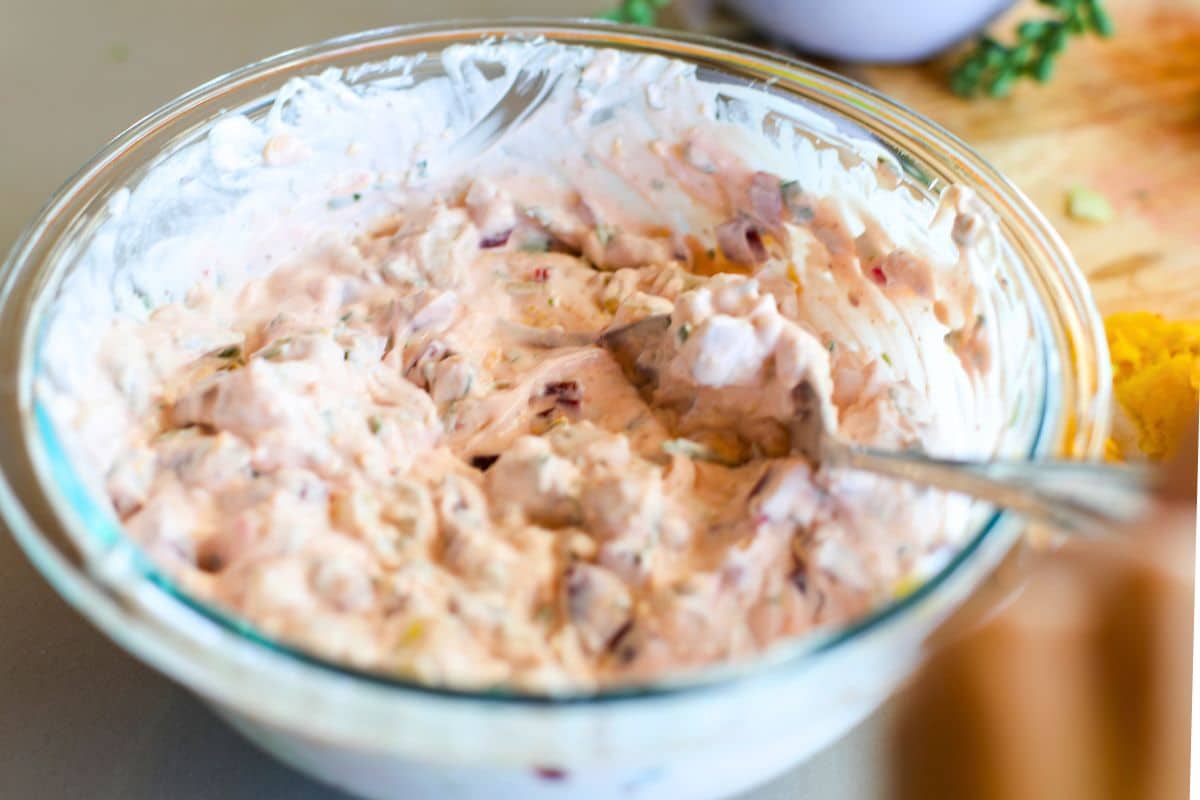A glass bowl filled with a creamy Beetroot Raita being stirred with a spoon, sitting on a kitchen counter.