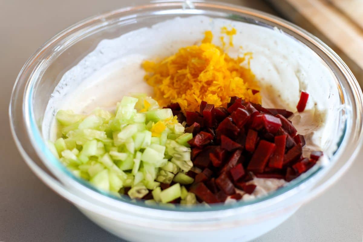 A glass bowl containing Greek yogurt topped with chopped cucumber, diced beetroot, and shredded carrots.