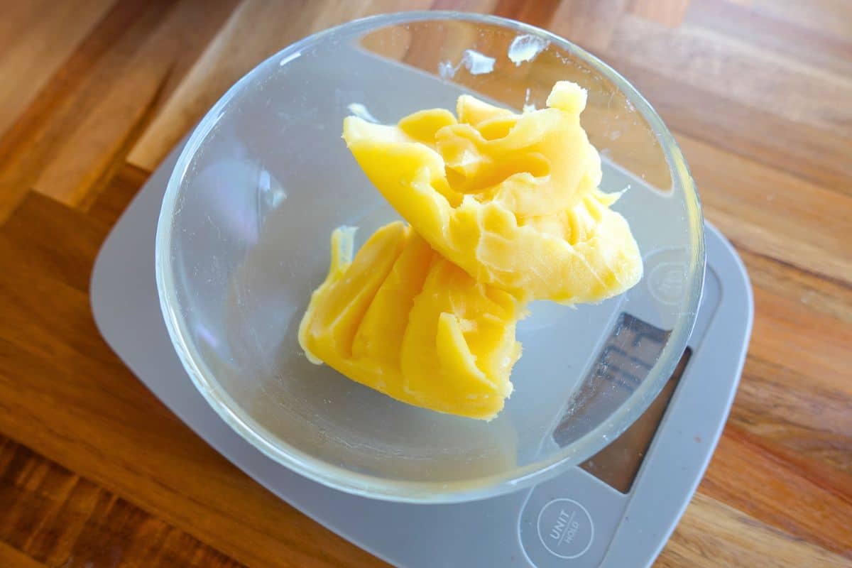 A glass bowl with a mound of ghee sitting on a digital kitchen scale on a wooden surface.