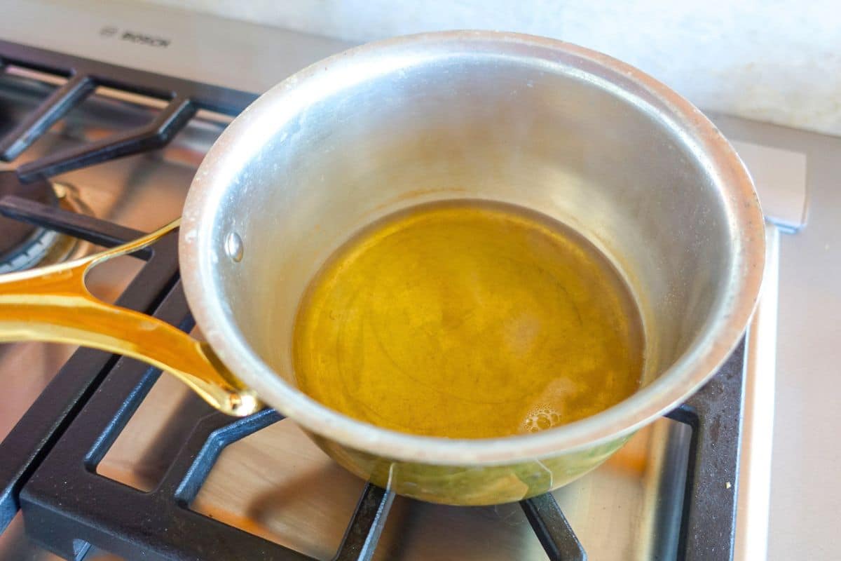 A small saucepan with melted ghee sits on a gas stove burner.