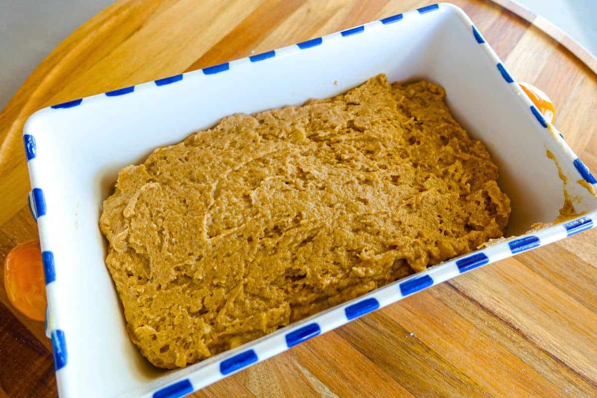 A rectangular ceramic baking dish filled with unbaked brown dough sits on a wooden surface.