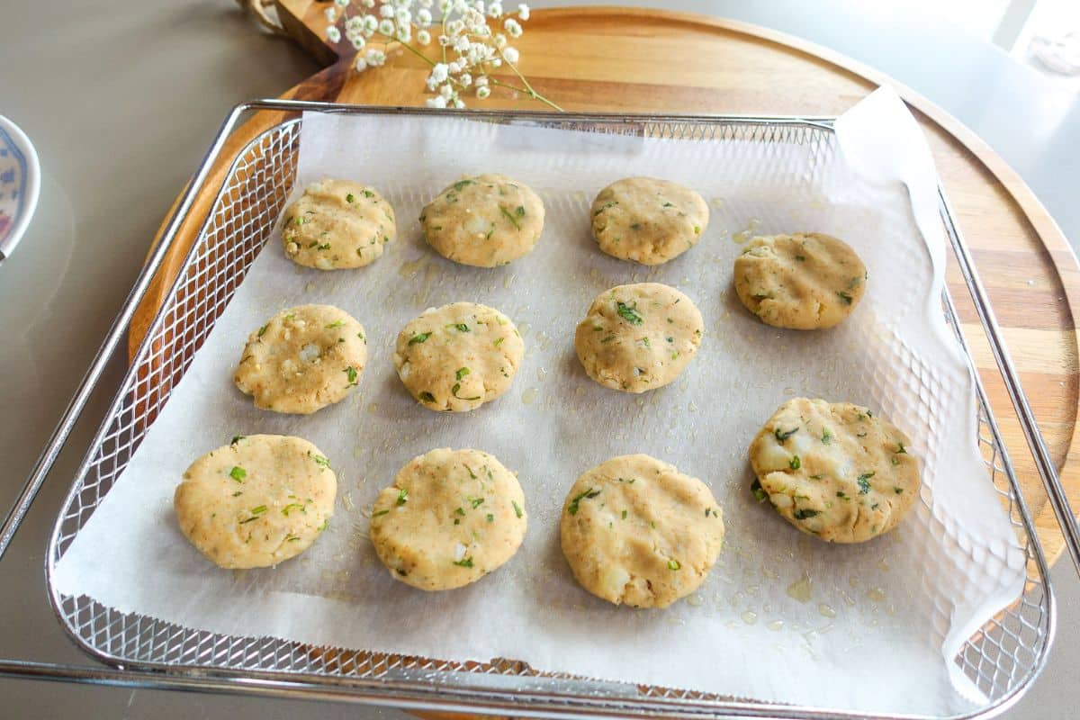 Unbaked round potato patties with herbs are arranged on parchment paper in a baking tray, ready for baking.