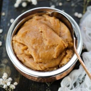A copper bowl filled with smooth, brown atta halwa, placed in a metal container.