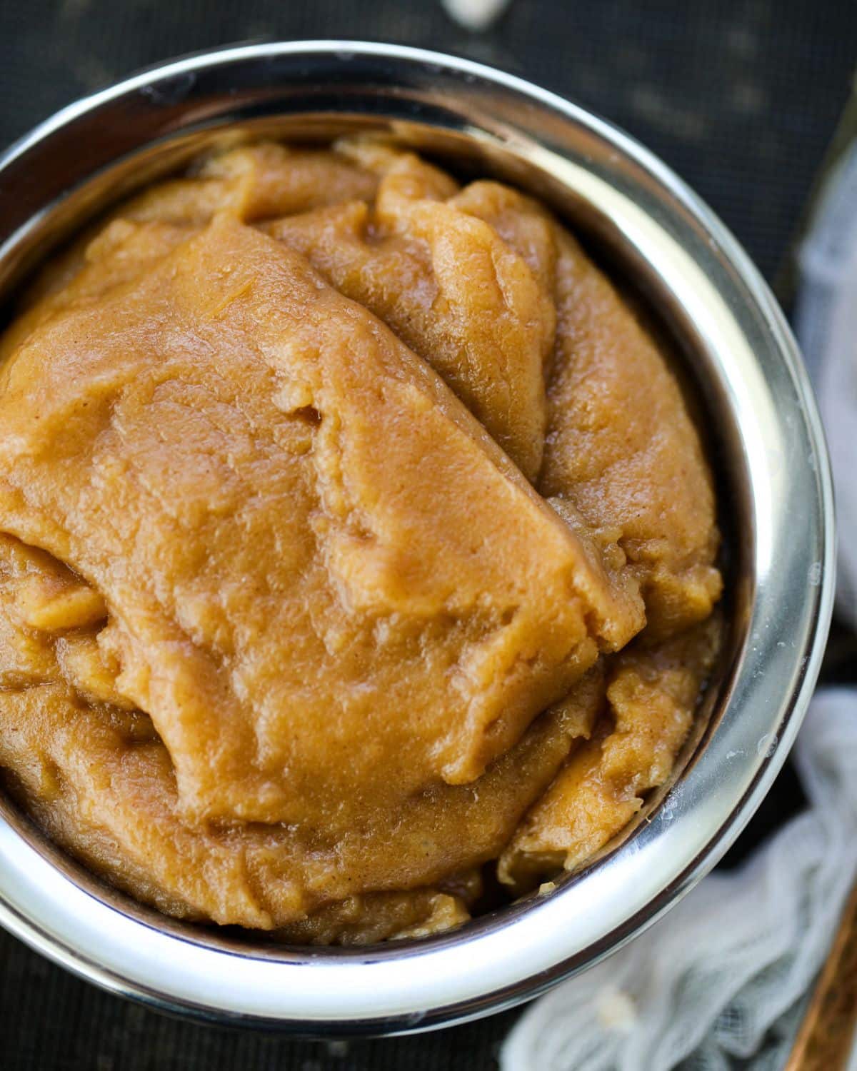 A stainless steel bowl filled with thick, brown atta halwa placed on a dark surface.