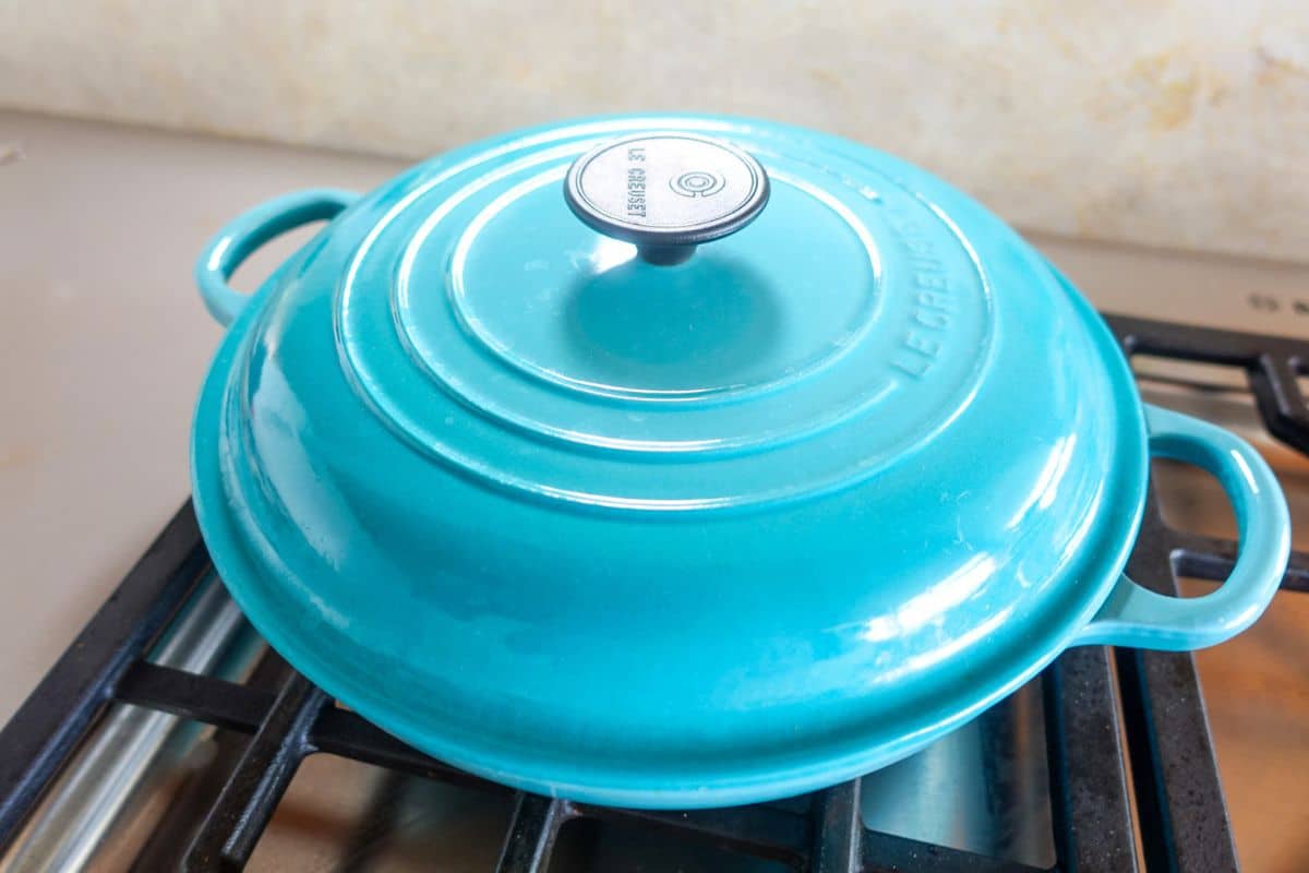 A closed turquoise Le Creuset Dutch oven sits on a stovetop burner.