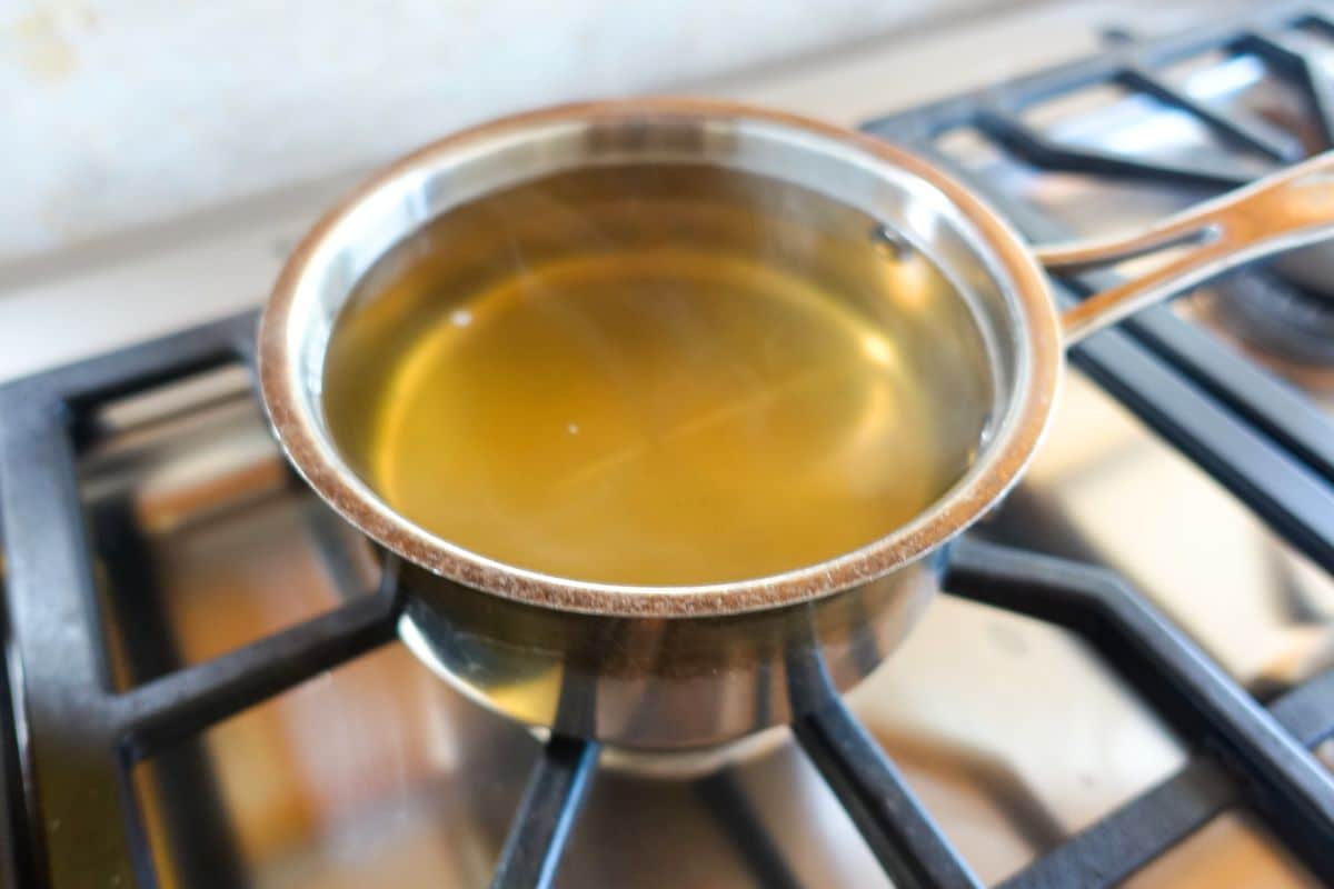 A metal saucepan filled with clear sugar syrup is heating on a gas stove burner.