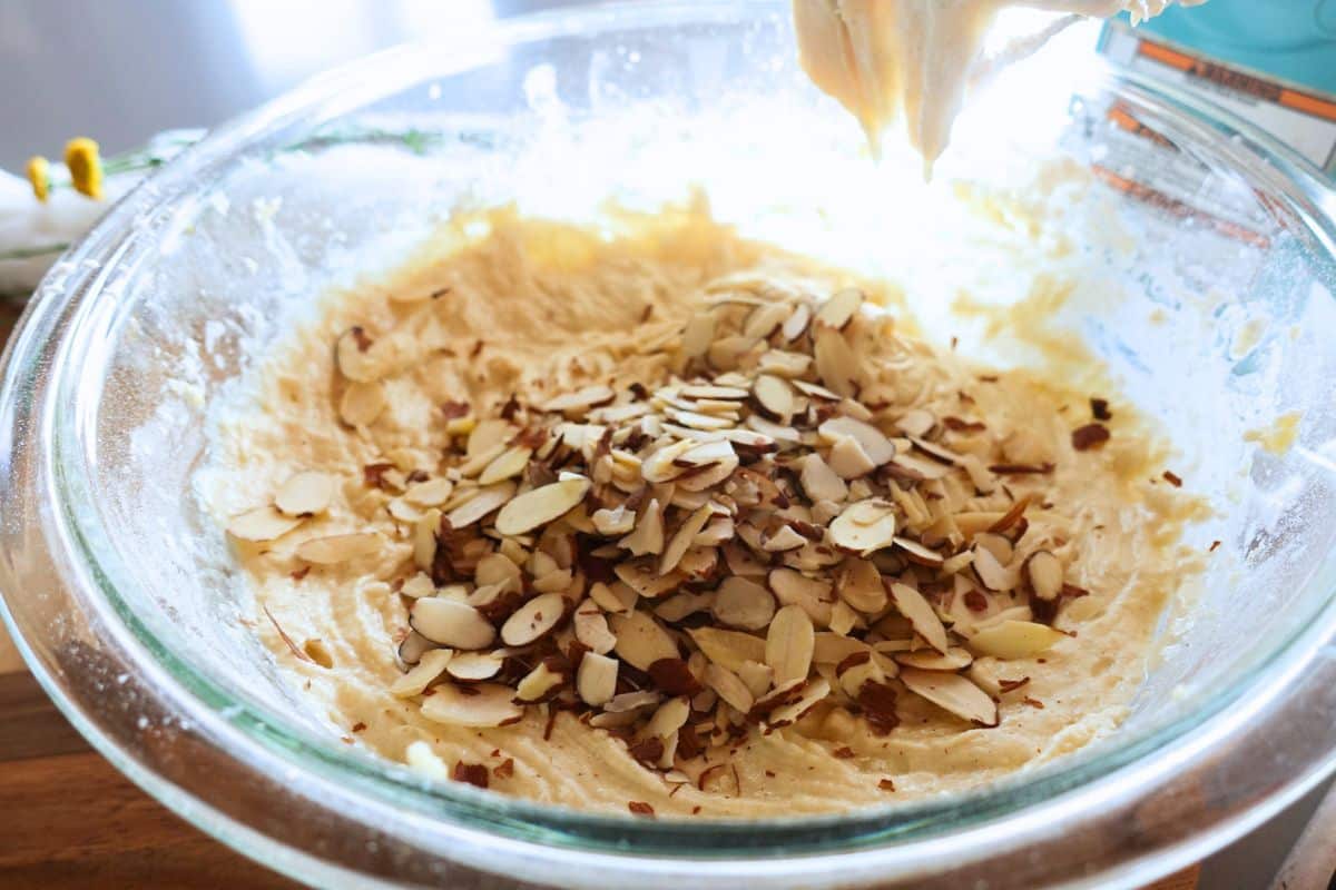 Sliced almonds being folded into cookie dough in a glass mixing bowl.