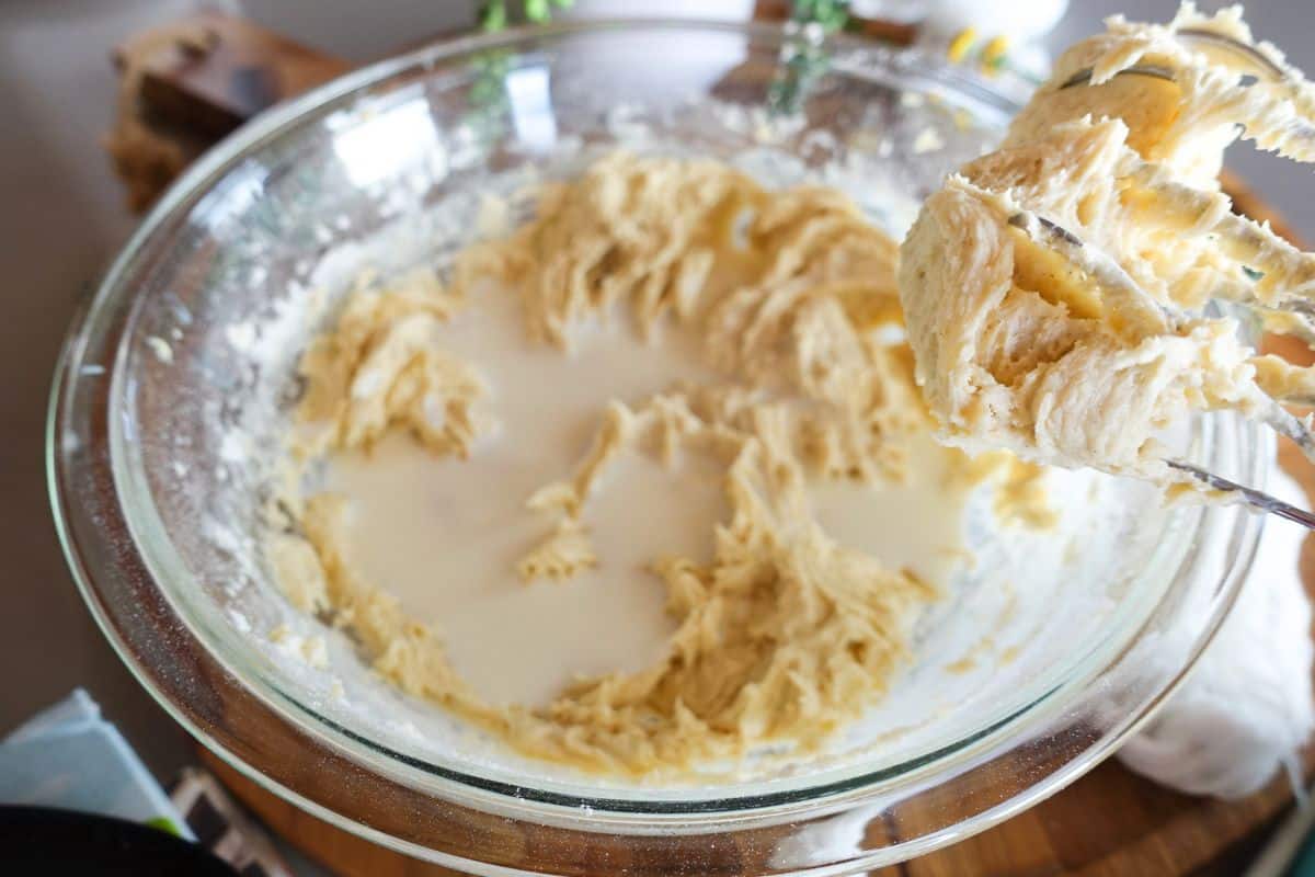 Cake batter with milk in a glass mixing bowl with an electric beater attachment held to the side.