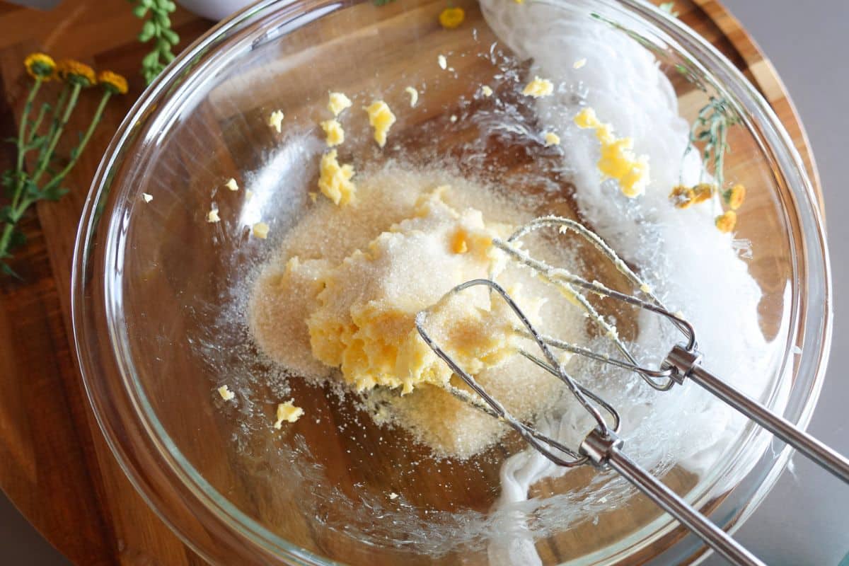 Electric beaters creaming butter and granulated sugar in a glass bowl.