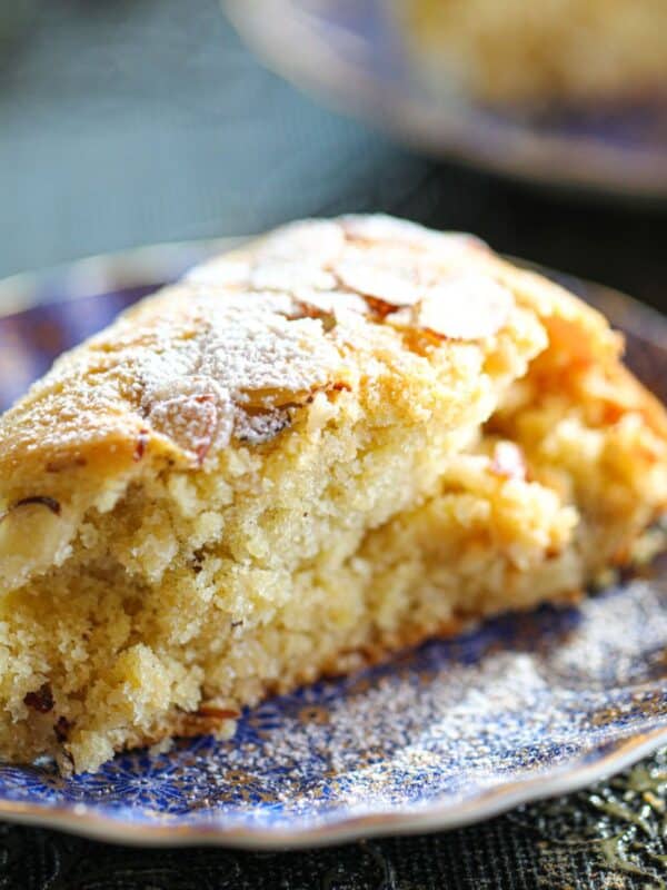 A slice of almond cake topped with powdered sugar and sliced almonds on a patterned blue plate.