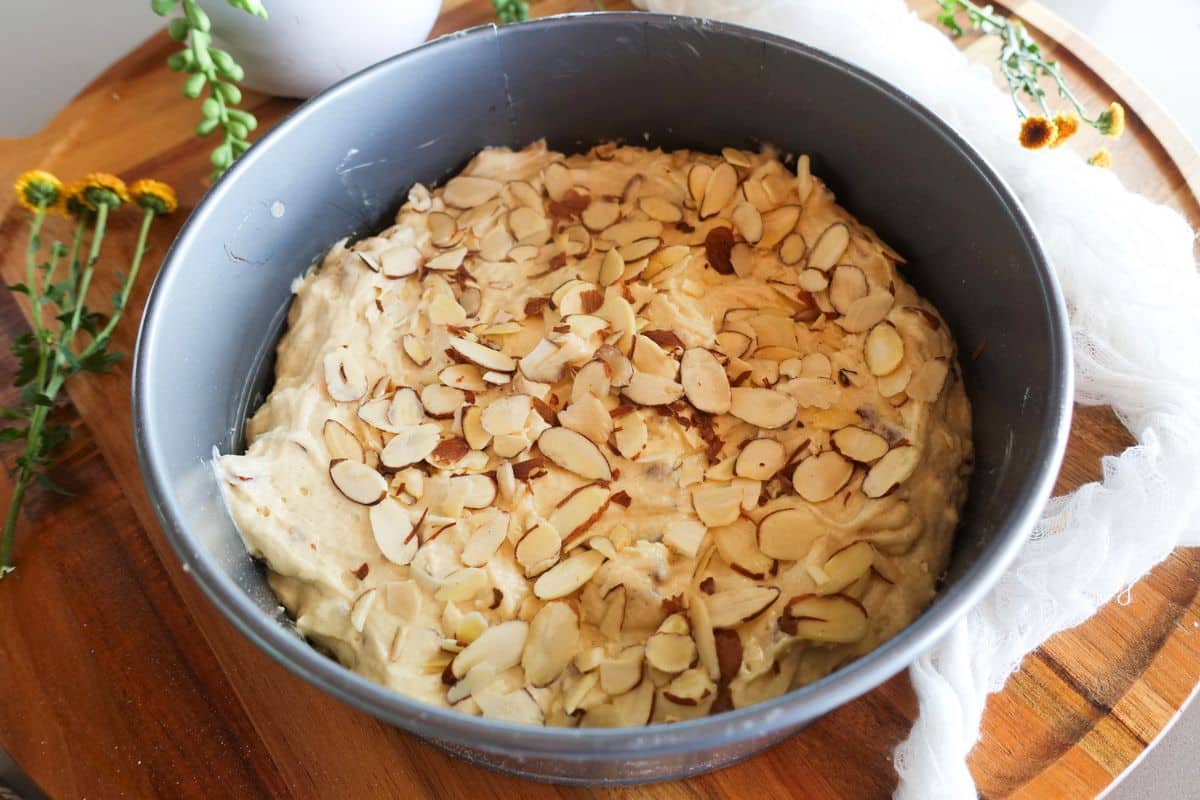 Cake batter in a round metal pan, topped with sliced almonds.